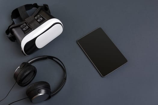 Virtual reality glasses and tablet with headphones on a gray background. Top view. Copy space