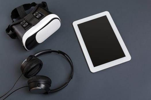 Virtual reality glasses and tablet with headphones on a gray background. Top view. Copy space