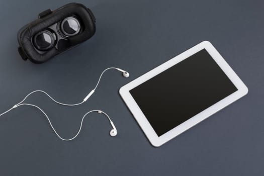 Virtual reality glasses and tablet with headphones on a gray background. Top view. Copy space
