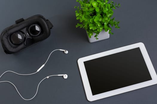 Virtual reality glasses and tablet with headphones on a gray background. Top view. Copy space