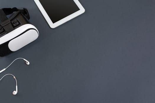 Virtual reality glasses and tablet with headphones on a gray background. Top view. Copy space