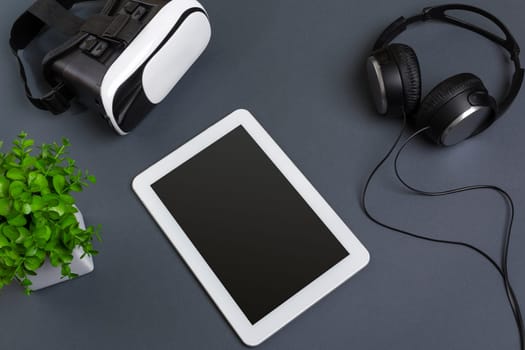 Virtual reality glasses and tablet with headphones on a gray background. Top view. Copy space