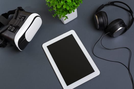 Virtual reality glasses and tablet with headphones on a gray background. Top view. Copy space