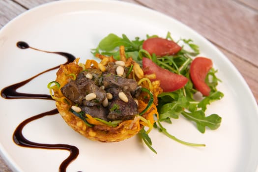 Recipe for poultry giblets in a nest of fried potatoes with rocket and tomato salad. High quality photo