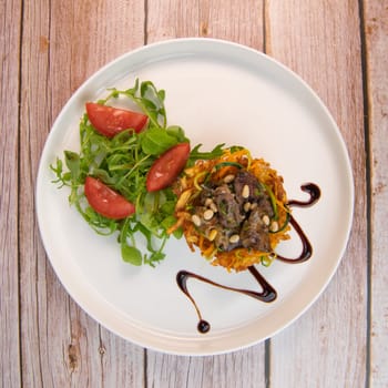 Recipe for poultry giblets in a nest of fried potatoes with rocket and tomato salad. High quality photo