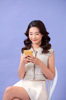 Asian woman sitting on chair using her phone with a happy expression