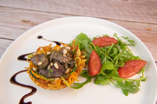 Recipe for poultry giblets in a nest of fried potatoes with rocket and tomato salad. High quality photo