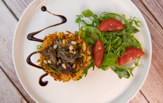 Recipe for poultry giblets in a nest of fried potatoes with rocket and tomato salad. High quality photo