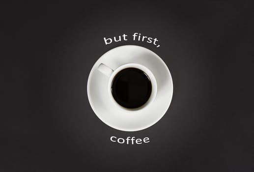 Coffee in white cup with a lettering But first coffee on black slate background, top view