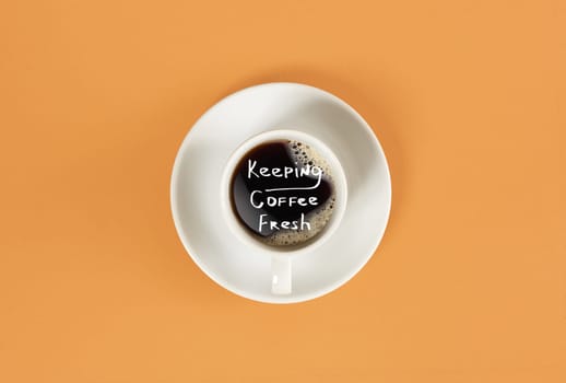 Top view of cup of black coffee and Keeping coffee fresh lettering isolated on orange background. Still life. Mock up. Flat lay