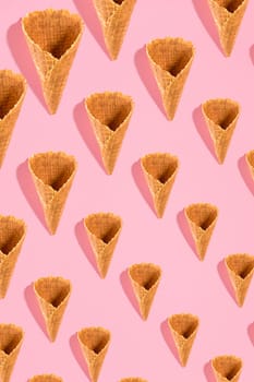 Sugar waffle cone for ice cream arranged in pattern on pink background. The image with copy space can be used as a background for the design of the confectionery menu, cards, greetings, invitations, pattern