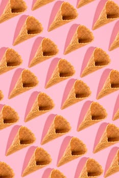 Sugar waffle cone for ice cream arranged in pattern on pink background. The image with copy space can be used as a background for the design of the confectionery menu, cards, greetings, invitations, pattern