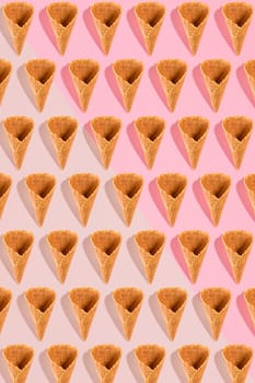 Sugar waffle cone for ice cream arranged in pattern on pink background. The image with copy space can be used as a background for the design of the confectionery menu, cards, greetings, invitations, pattern