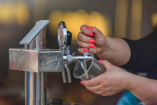 The bartender pours craft beer from the tap into a glass. The hand at the beer tap pours draft beer into a glass at the bar