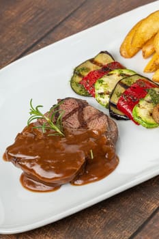 Grilled beef tenderloin with bolognese sauce with grilled vegetables on a white porcelain plate