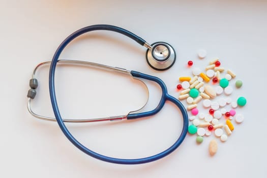 Stethoscope with pile of colorful antibiotic capsule pills on white table with drug tray. Antimicrobial drug resistance and overuse. Medical equipment