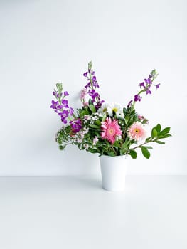 bouquet of flowers in a white vase. japanese dianthus, gerbera, matthiola, chamomile and laurel leaves. flower arrangement with empty space for text or inscription. spring postcard. photography in daylight.