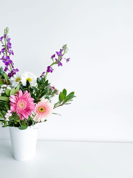 bouquet of flowers in a white vase. japanese dianthus, gerbera, matthiola, chamomile and laurel leaves. flower arrangement with empty space for text or inscription. spring postcard. photography in daylight.