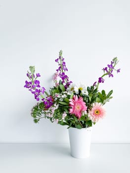bouquet of flowers in a white vase. japanese dianthus, gerbera, matthiola, chamomile and laurel leaves. flower arrangement with empty space for text or inscription. spring postcard. photography in daylight.