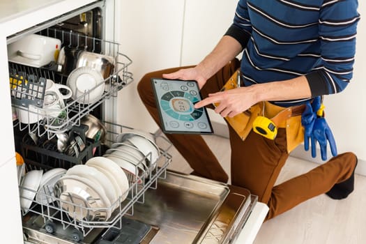 Portrait Of Male Technician Repairing Dishwasher In Kitchen using digital tablet