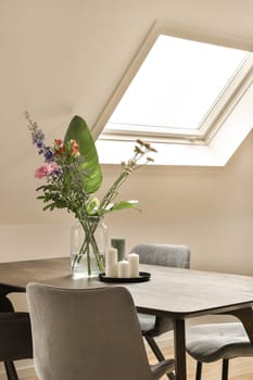 some flowers in a vase on top of a wooden table with chairs and a skylight above the dining area