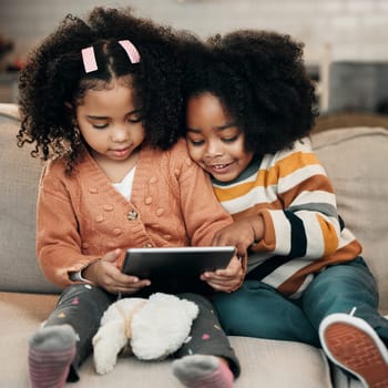 Happy children on sofa with tablet for online education, fun games and watch internet cartoon or video together. Biracial family kids on couch with digital technology, app or web for movie streaming.