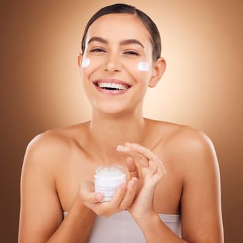 Portrait, skincare and cream with a model woman in studio on a brown background for beauty or hydration. Face, beauty and product with a happy young female holding a container to apply moisturizer.