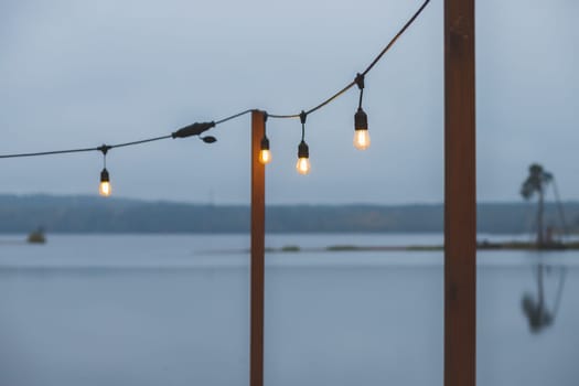 Twilight, gray color sky at the lakescape, electric lamps as garland and wooden terrace, pier.