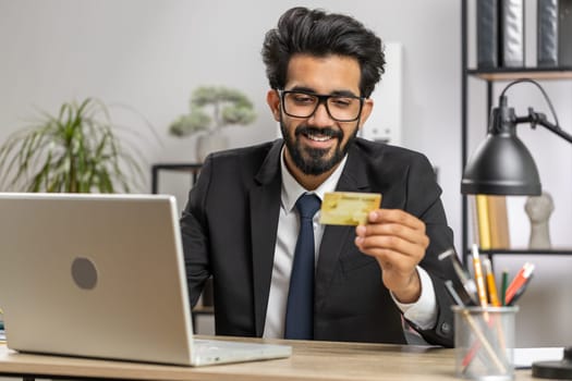 Bearded businessman programmer software developer working making online purchase payment shopping with credit bank card and use laptop at home office desk with laptop. Indian freelancer business man