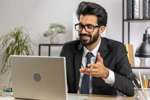 Indian businessman working on laptop computer at home office desk talk on online communication video call with employee, boss. Manager man freelancer support services looking at webcam of computer