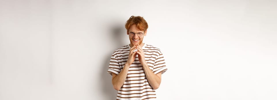 Portrait of redhead man looking like evil genius, steeple fingers and chuckling devious, scheming some plan, standing over white background.