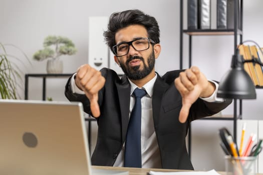 Dislike. Upset indian businessman guy working on laptop computer at home office thumbs down sign gesture, expressing discontent, disapproval, dissatisfied bad work. Displeased serious freelancer man