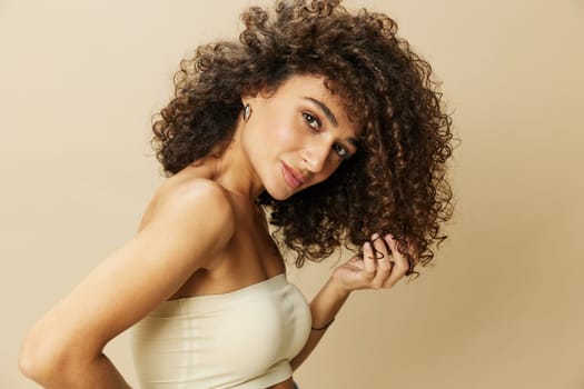 Woman applies cream and balm to her curly hair, the concept of protection and care, a healthy look, a smile with teeth on a beige background.