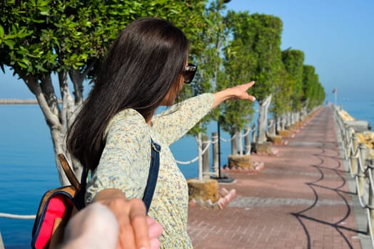 A young woman in a dress points the direction to the sea with her hand. Pier at the beach of Sharjah UAE