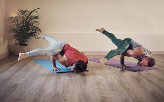 We push our bodies to the limit. Full length shot of two young men holding an extended side crow pose during an indoor yoga session together