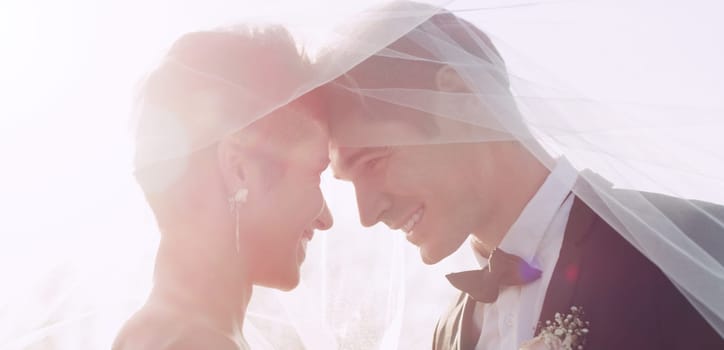 Love is such a beautiful place to be in. an affectionate young newlywed couple smiling at each other while covering themselves with a veil on their wedding day