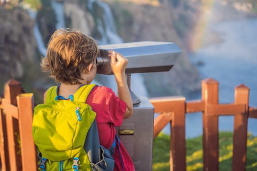 Boy tourist with a backpack on the background of Duden waterfall in Antalya. Famous places of Turkey. Lower Duden Falls drop off a rocky cliff falling from about 40 m into the Mediterranean Sea in amazing water clouds. Tourism and travel destination photo in Antalya, Turkey. Turkiye.