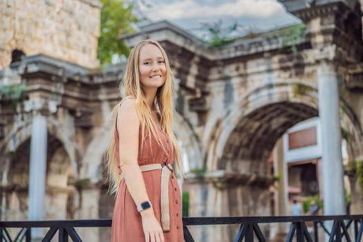 Happy female tourist traveler discover interesting places and popular attractions and walks in the old city of Antalya. Hadrian Kapisi turkey landmark city history. Popular tourist attraction - ancient Roman Hadrian Gate in old town Antalya, Turkey on a summer day. Turkiye.