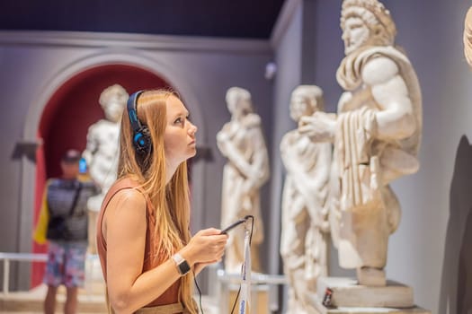 Portrait of contemporary young woman looking at sculptures and listening to audio guide at museum exhibition.