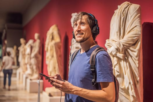 Portrait of contemporary man looking at sculptures and listening to audio guide at museum exhibition.