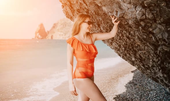 Young woman in red bikini on Beach. Blonde in sunglasses on pebble beach enjoying sun. Happy lady in one piece red swimsuit relaxing and sunbathing by turquoise sea ocean on hot summer day. Close up,