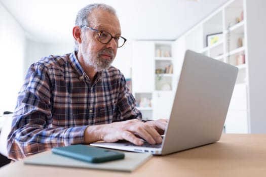 Mature caucasian adult man working with laptop at home. Technology.