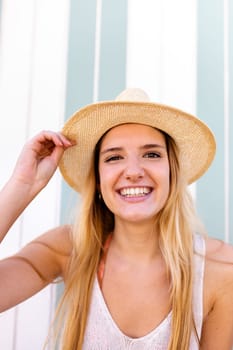 Headshot of young happy blond woman on vacation wearing hat looking at camera. Vertical portrait.