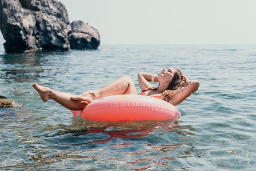 Woman summer sea. Happy woman swimming with inflatable donut on the beach in summer sunny day, surrounded by volcanic mountains. Summer vacation concept