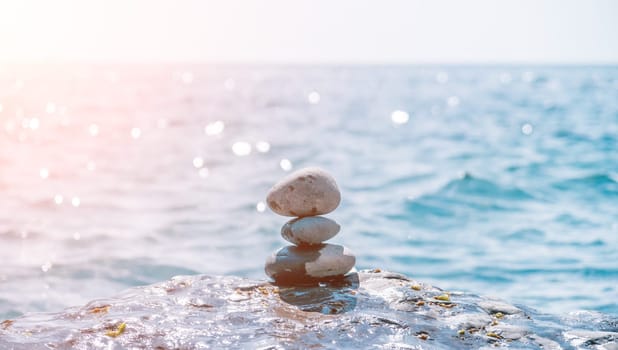 Balanced Pebbles Pyramid on the Beach on Sunny Day and Clear Sky at Sunset. Blue Sea on Background Selective focus, zen stones on sea beach, meditation, spa, harmony, calm, balance concept.