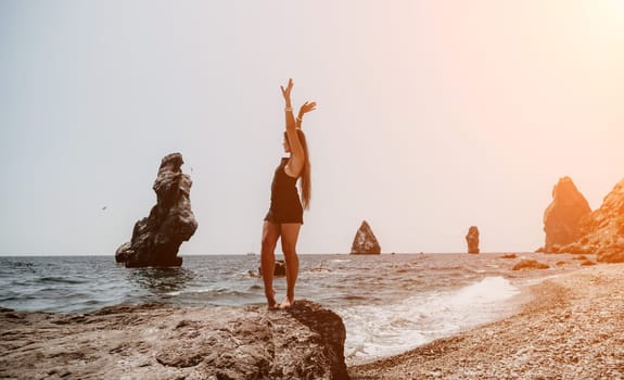 Woman travel sea. Young Happy woman in a long red dress posing on a beach near the sea on background of volcanic rocks, like in Iceland, sharing travel adventure journey