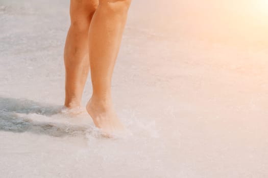 Sea beach travel - woman walking on sand beach leaving footprints in the white sand. Female legs walking along the seaside barefoot, close-up of the tanned legs of a girl coming out of the water