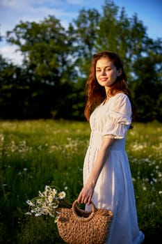 portrait of a beautiful red-haired girl in a light summer dress in nature with a basket of flowers. High quality photo