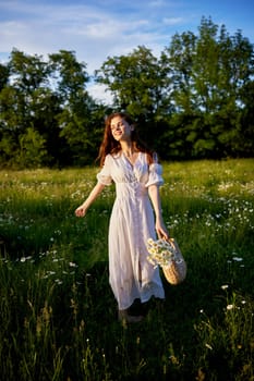 a beautiful, happy woman in a light dress stands in a chamomile field in the rays of the setting sun. High quality photo