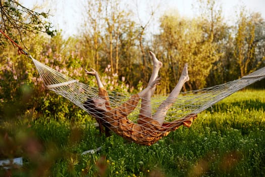 a funny woman is resting in nature lying in a mesh hammock in a long orange dress lifting up her arms and legs. High quality photo